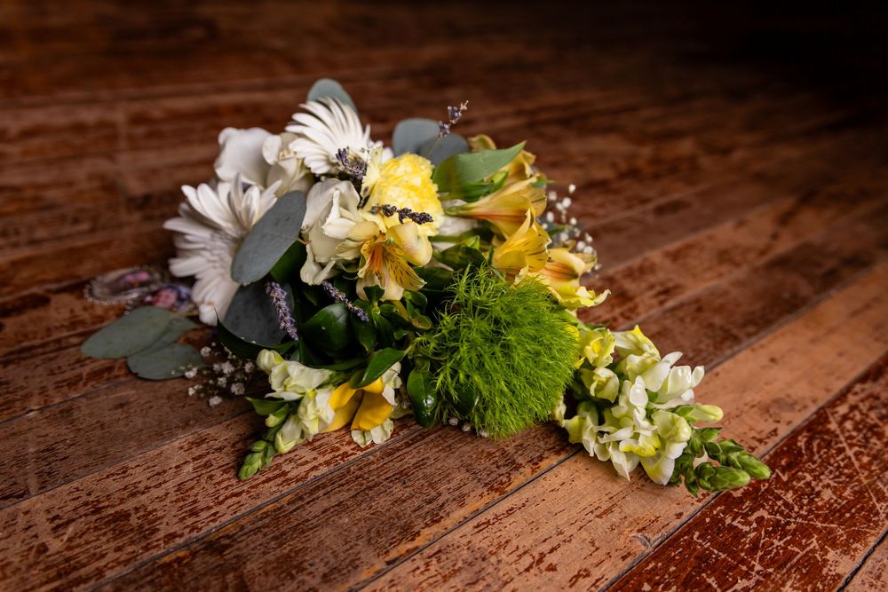 Yellow and white floral bouquet with green accents resting on a rustic wooden surface.