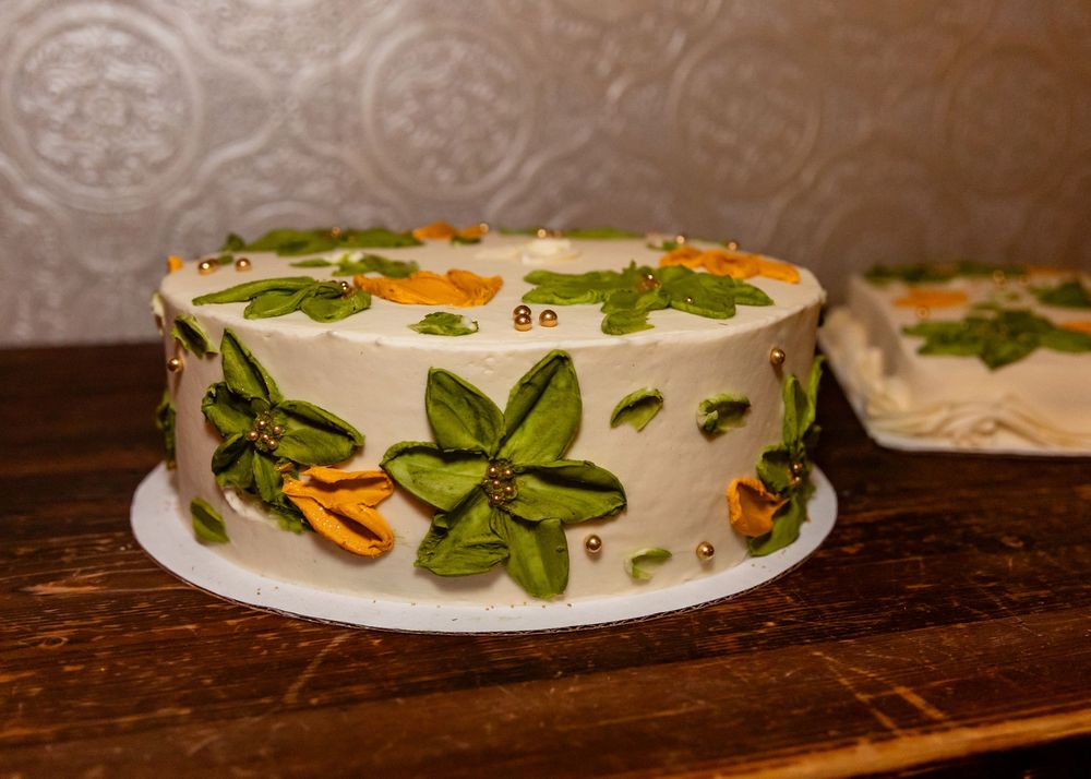 White frosted cake decorated with green fondant flowers and orange accents on a wooden surface.
