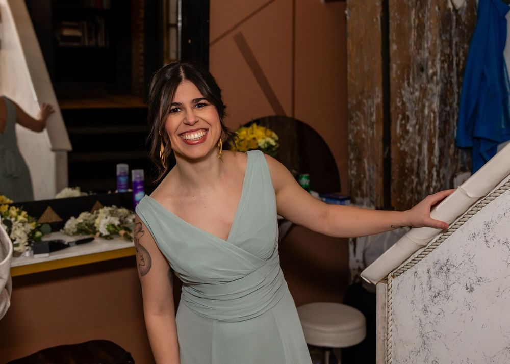 Smiling bridesmaid in sage green dress poses elegantly in a bridal suite getting ready room.