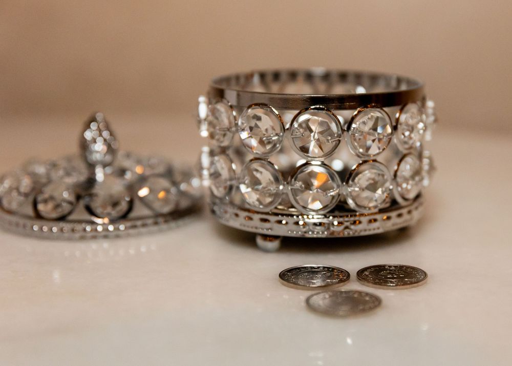 Silver crystal beaded jewelry box with lid and small coins on a white surface.