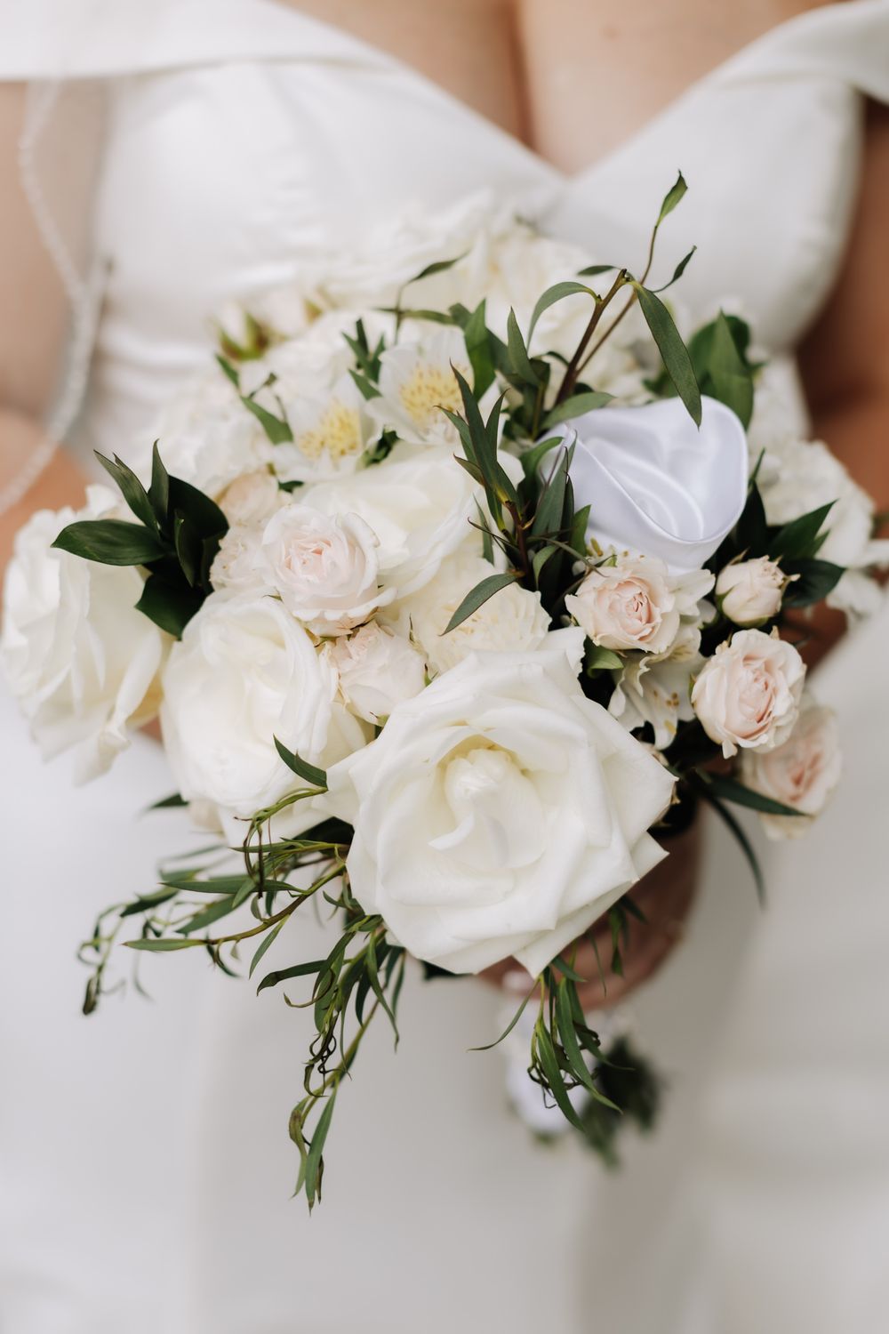Bride holding a romantic wedding bouquet of white and blush roses with greenery accents.