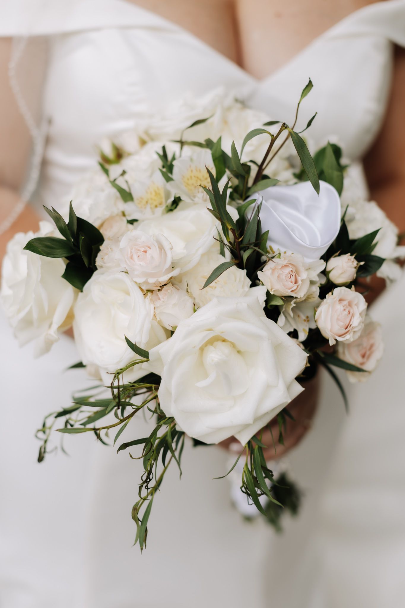 Bride holding a romantic wedding bouquet of white and blush roses with greenery accents.