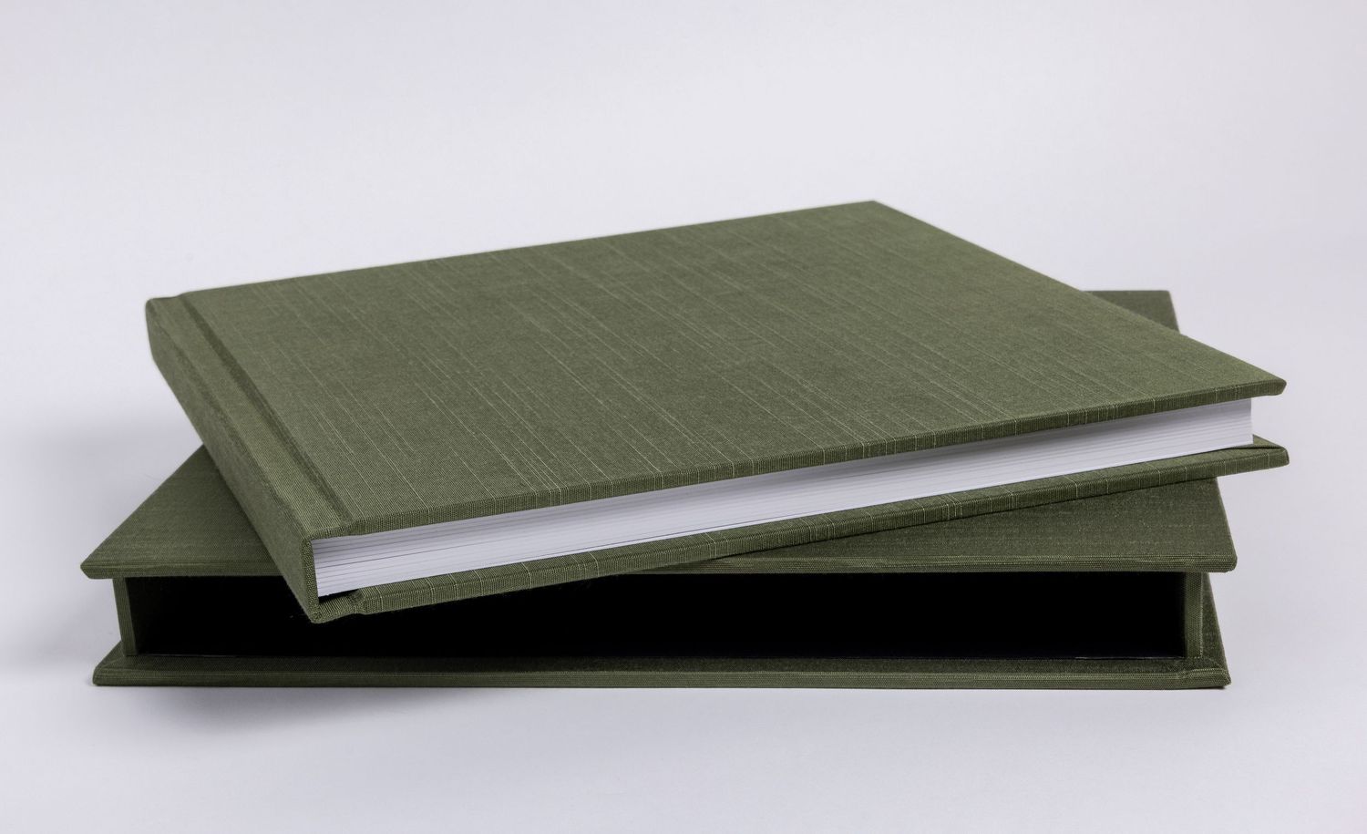 An olive green linen hardcover photo album with white pages.