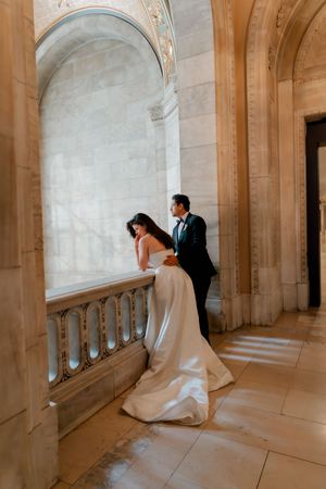 Elegant bride and groom sharing intimate moment at ornate marble balcony inside NYC Public Library.