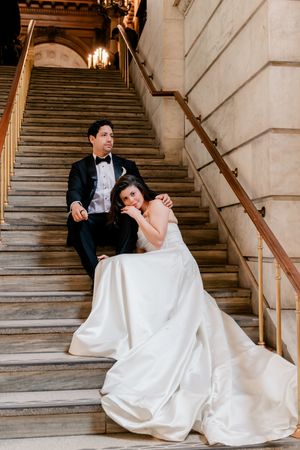 Bride and groom sitting on marble staircase steps in a grand classical building after wedding.