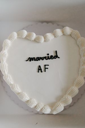 Heart-shaped white wedding cake decorated with frosting and black lettering reading married AF.