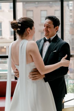 Groom in black tuxedo smiling at bride in white halter wedding dress during first look moment.