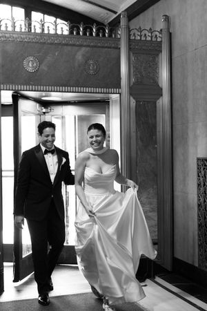 Black and white photo of joyful bride and groom entering an ornate building on their wedding day.