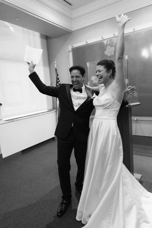Black and white photo of ecstatic newlyweds celebrating with raised arms after signing marriage license.