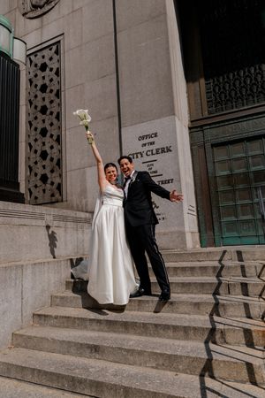 Joyful newlyweds celebrating on steps outside NYC City Clerk's Office after courthouse wedding ceremony.