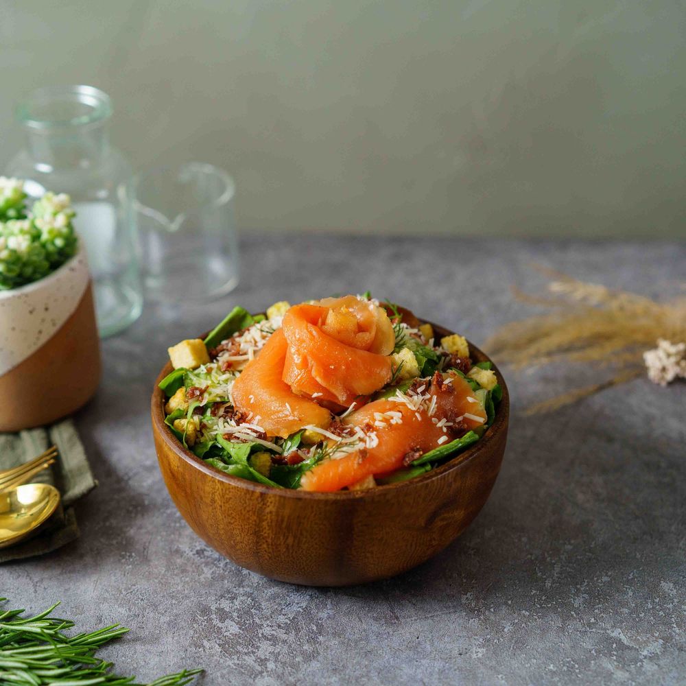 Fresh salmon poke bowl with avocado, seaweed and sesame seeds served in wooden bowl on gray surface.
