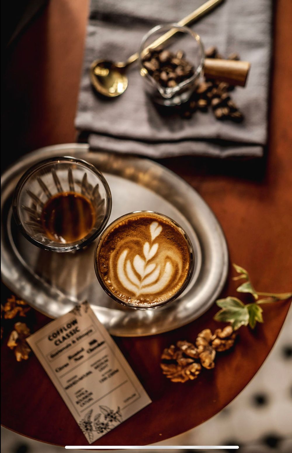 Overhead view of latte art with coffee beans, menu card and dried flowers on wooden table with moody lighting.