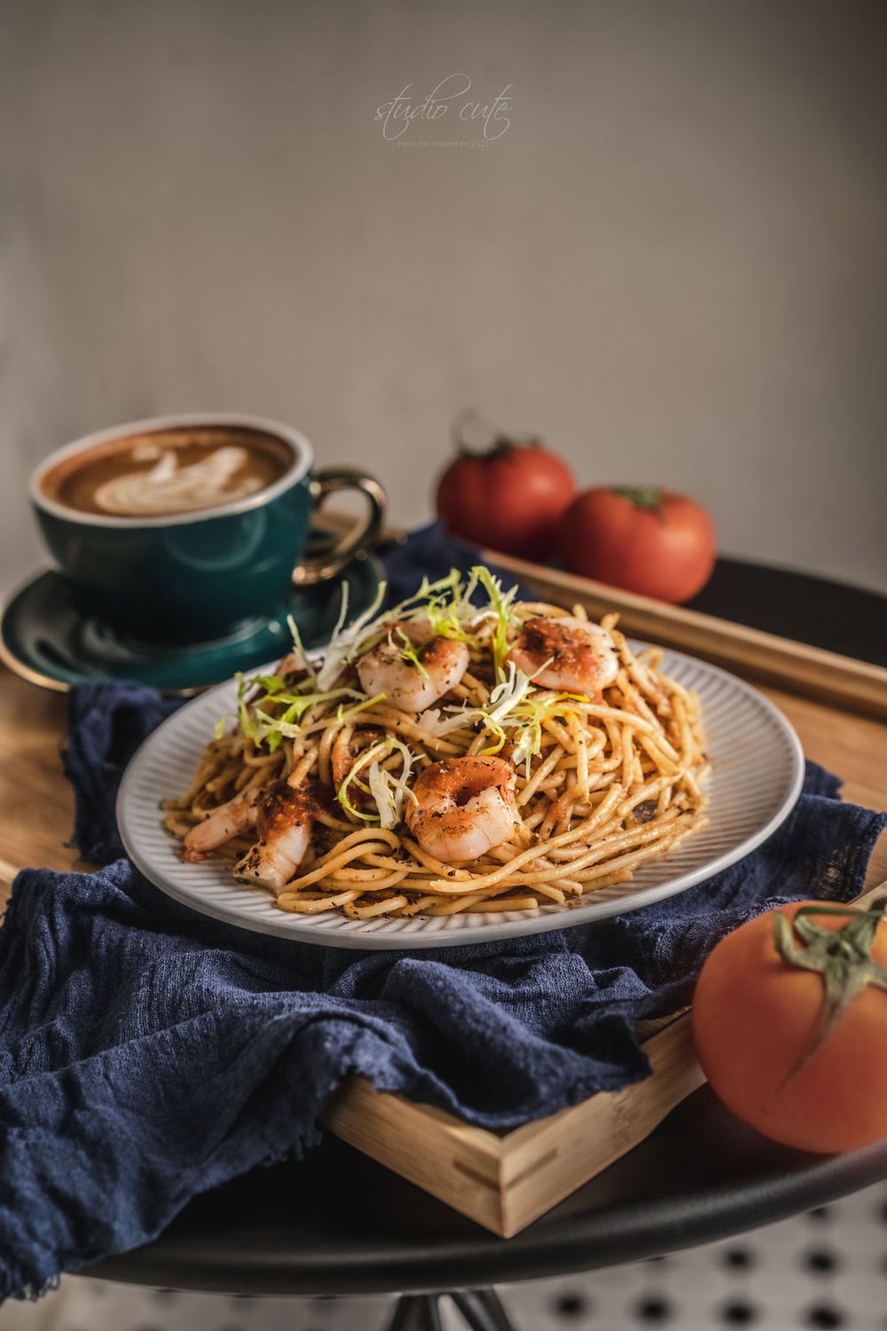 Homemade shrimp spaghetti with sprouts and tomatoes served on a plate with dark blue napkin in moody lighting.