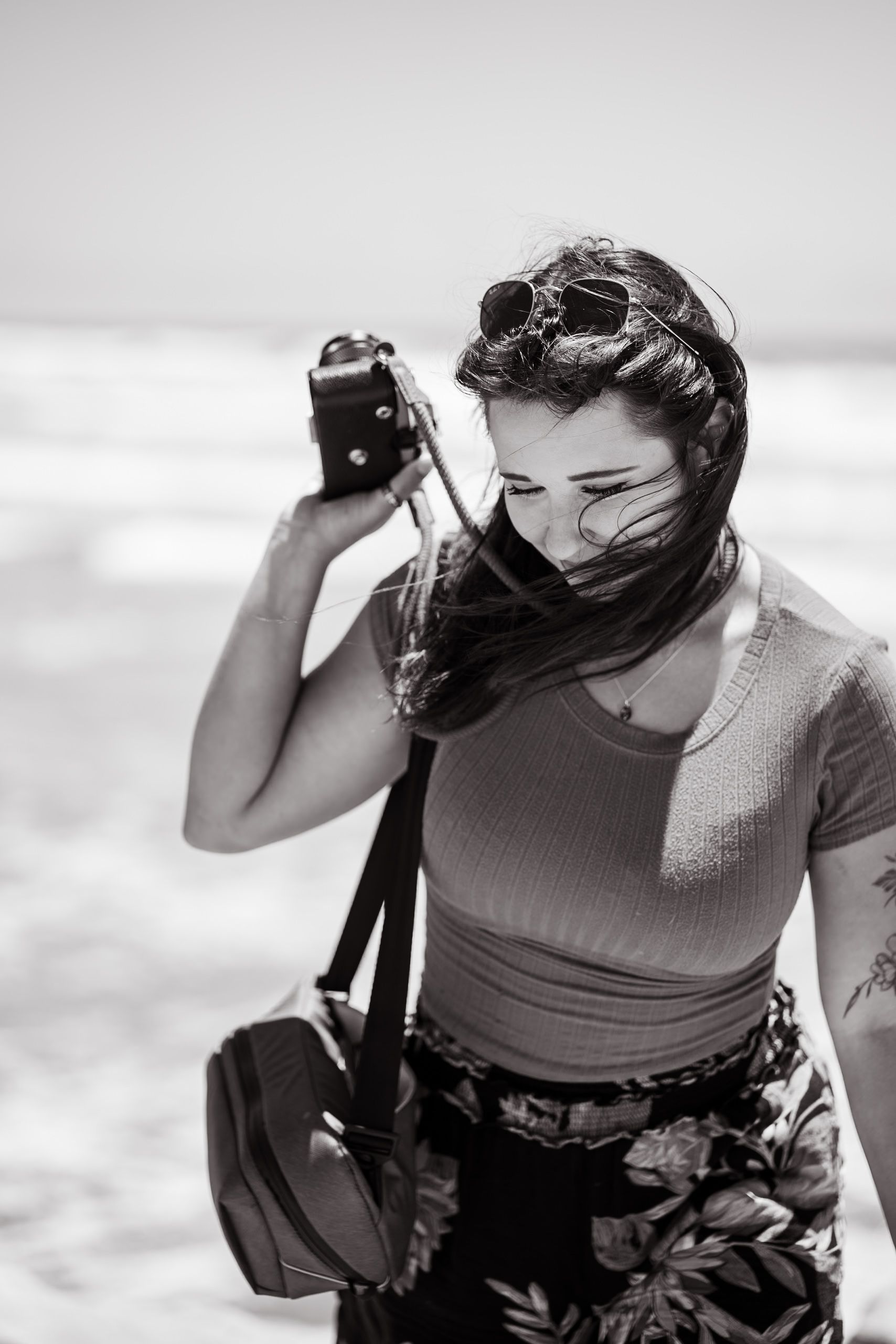 Southern California female beach photographer, looking down and smiling while holding film camera. Oceanside, CA