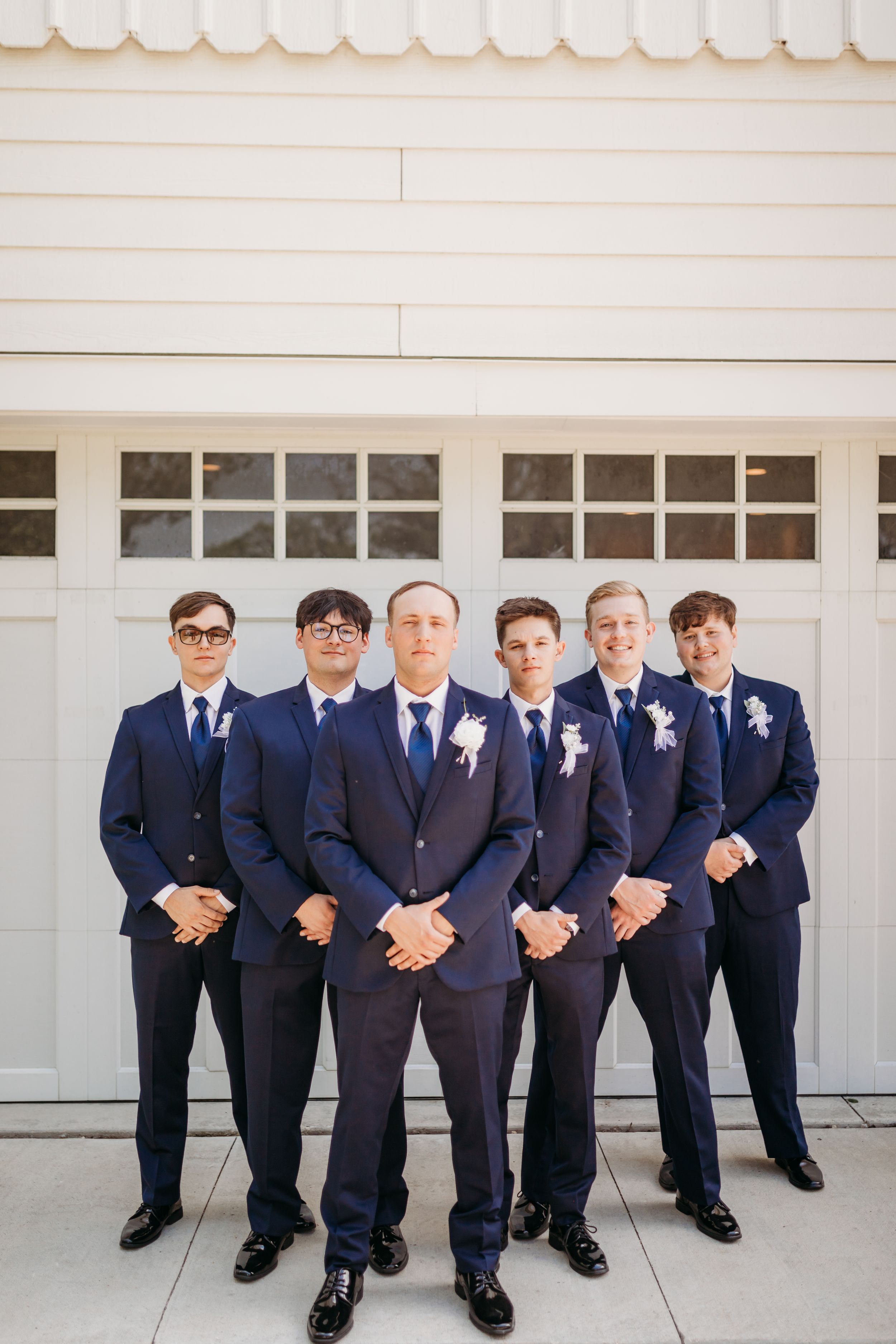 Groom and groomsmen in navy blue suits with boutonnieres posing in front of white garage doors.