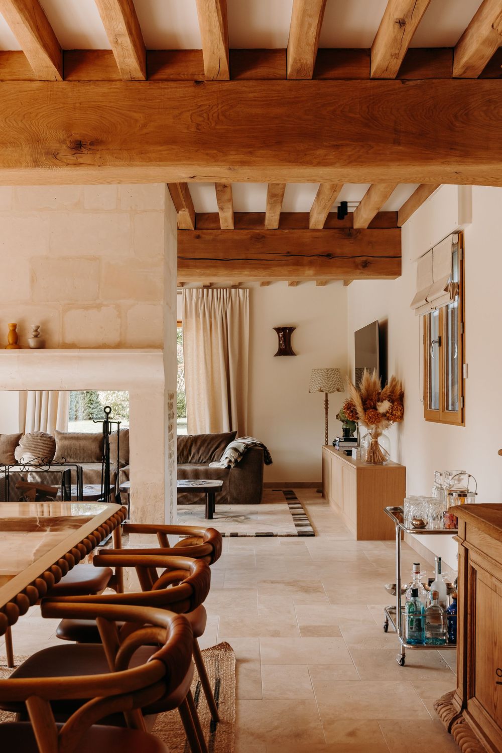 Rustic Mediterranean interior with exposed wooden beam ceiling, stone walls, leather chairs, and warm neutral tones throughout.