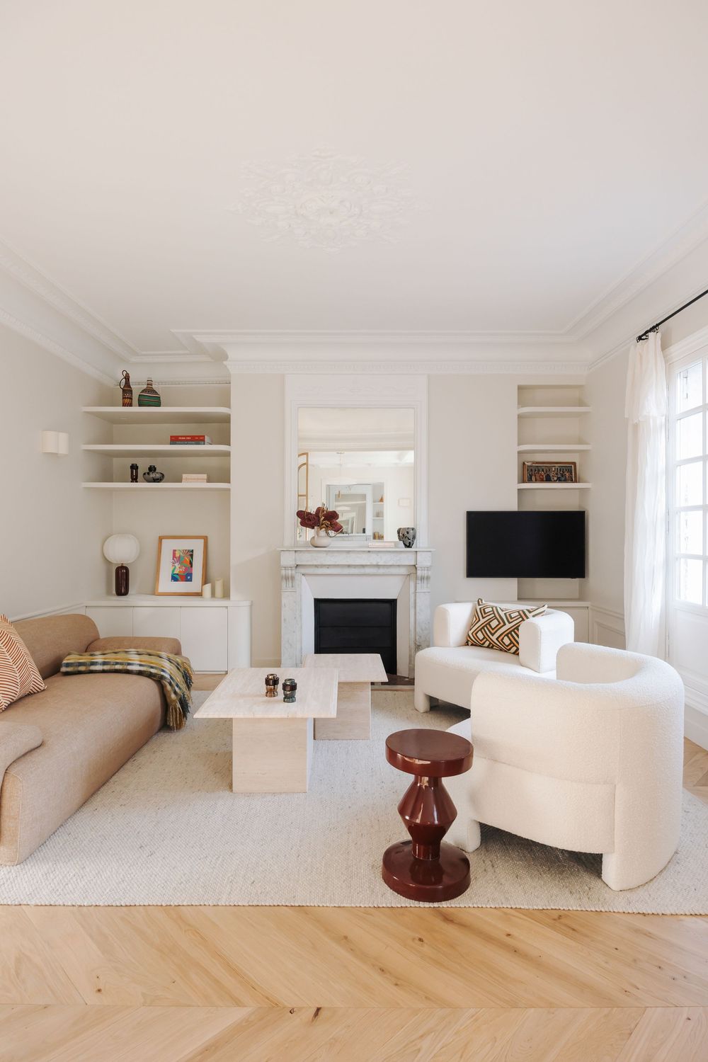 Elegant white living room with herringbone wood floors, built-in shelves, marble fireplace, cream sofa, and a walnut accent stool.