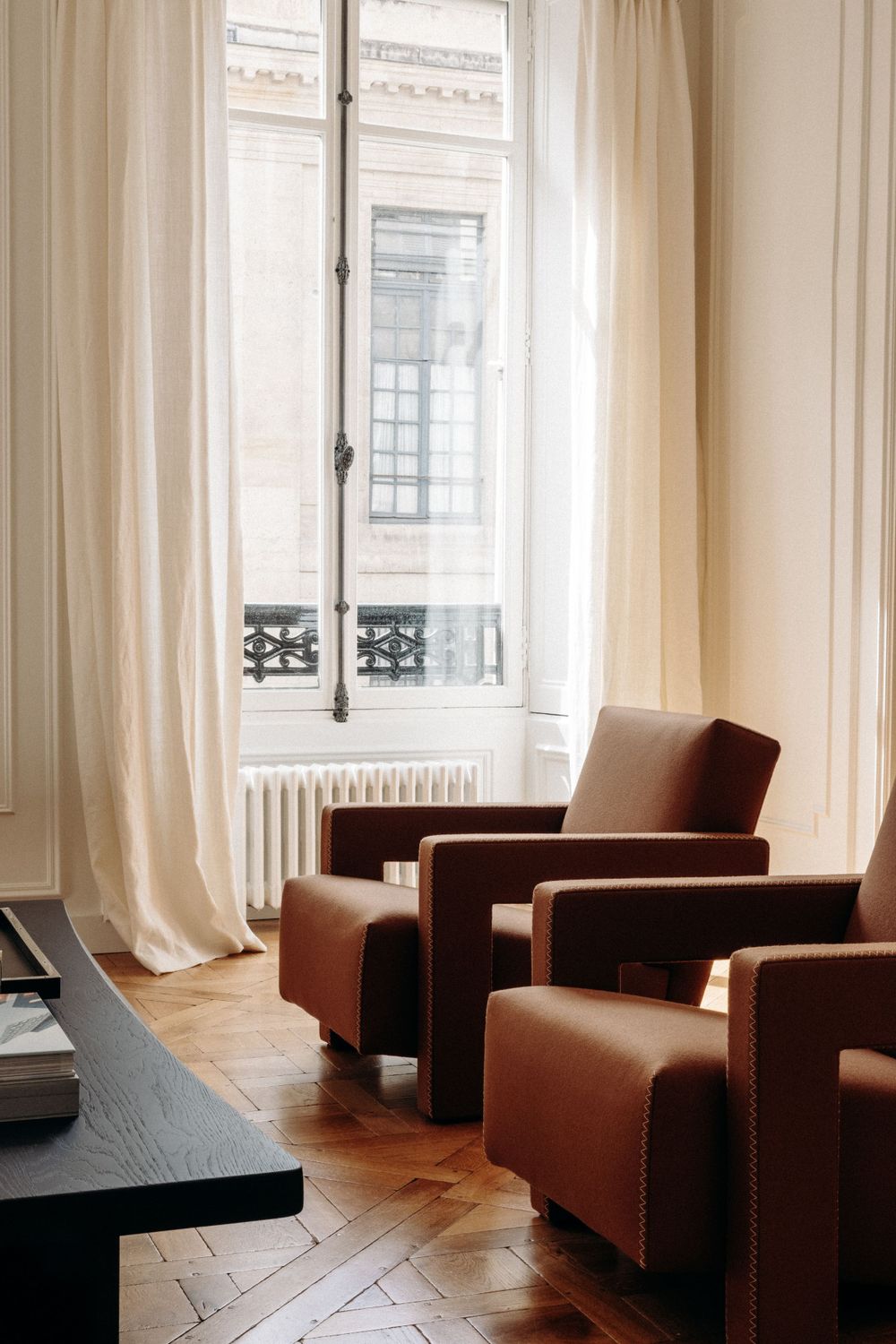 Elegant room interior with brown leather armchairs and floor-to-ceiling windows with sheer curtains.