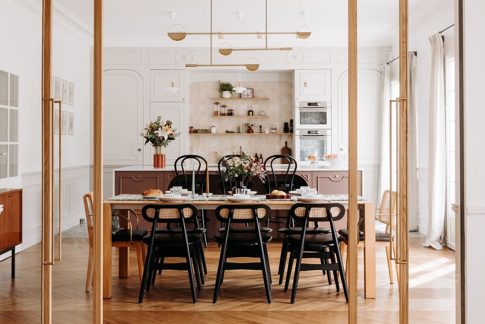 Elegant dining room with wooden table, black chairs, herringbone floors, open shelving, and gold pendant light.