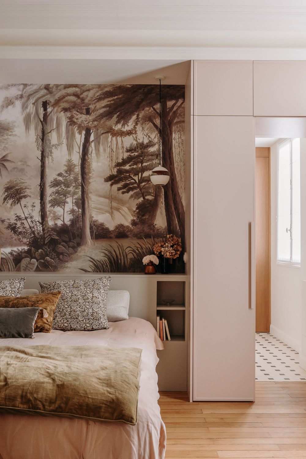 Elegant bedroom with tropical forest mural wallpaper, blush pink built-in wardrobe, and linen bedding on parquet floor.