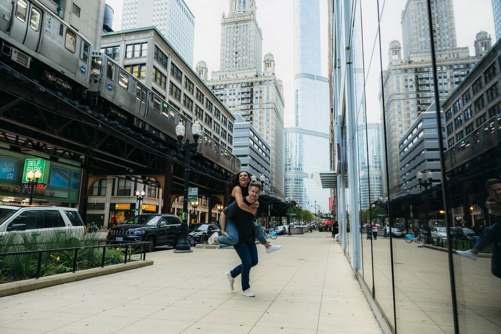 Couple joyfully dancing during engagement session on a Chicago city sidewalk with skyscrapers and elevated train tracks in the background.