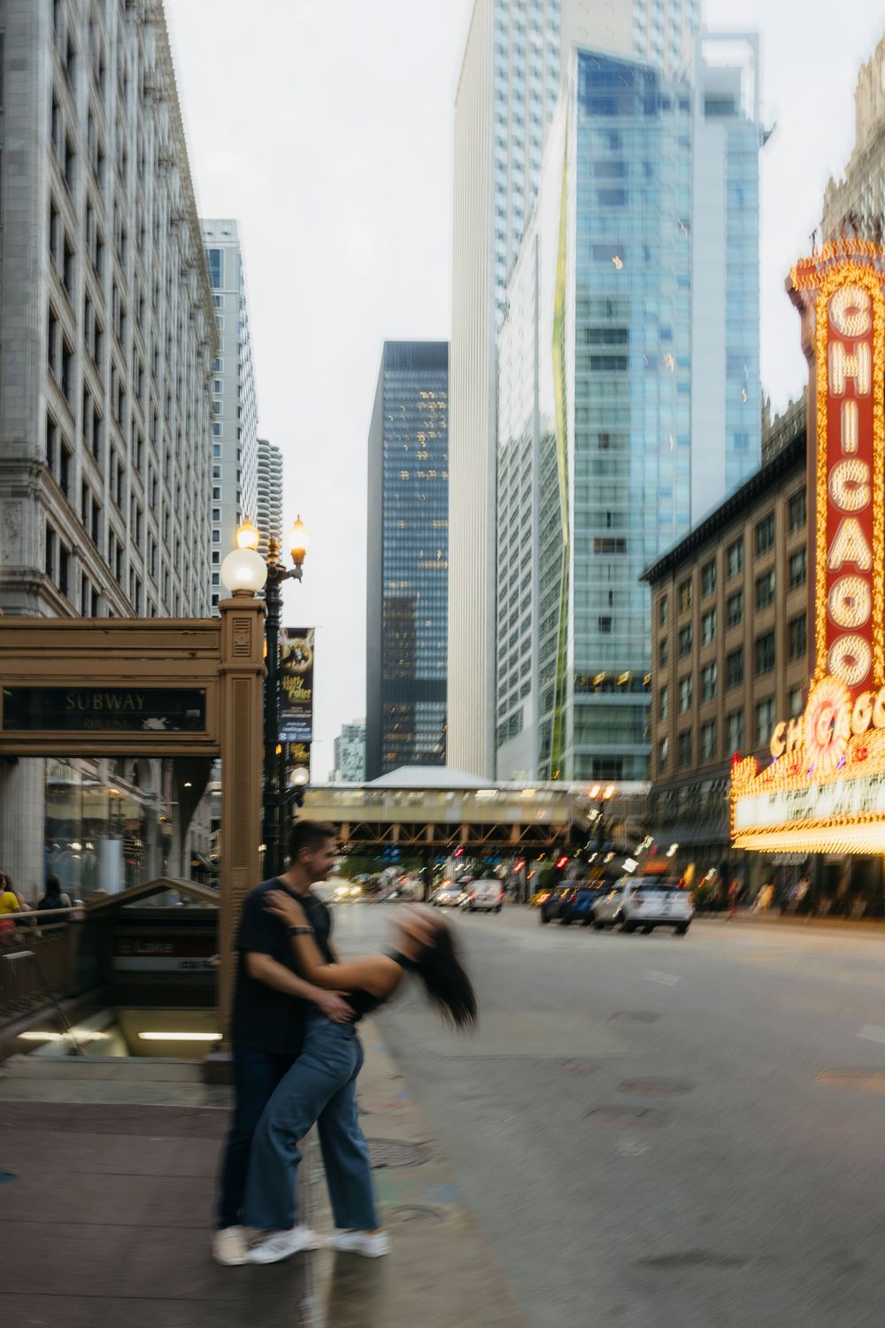 Couple dancing during engagement session on a busy Chicago street with the iconic Chicago Theatre marquee and skyscrapers in background.