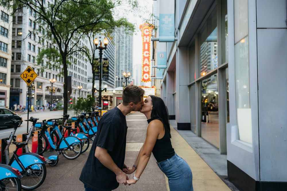 Couple kissing during engagement session in front of the iconic Chicago Theatre sign on State Street with Divvy bikes in the background.
