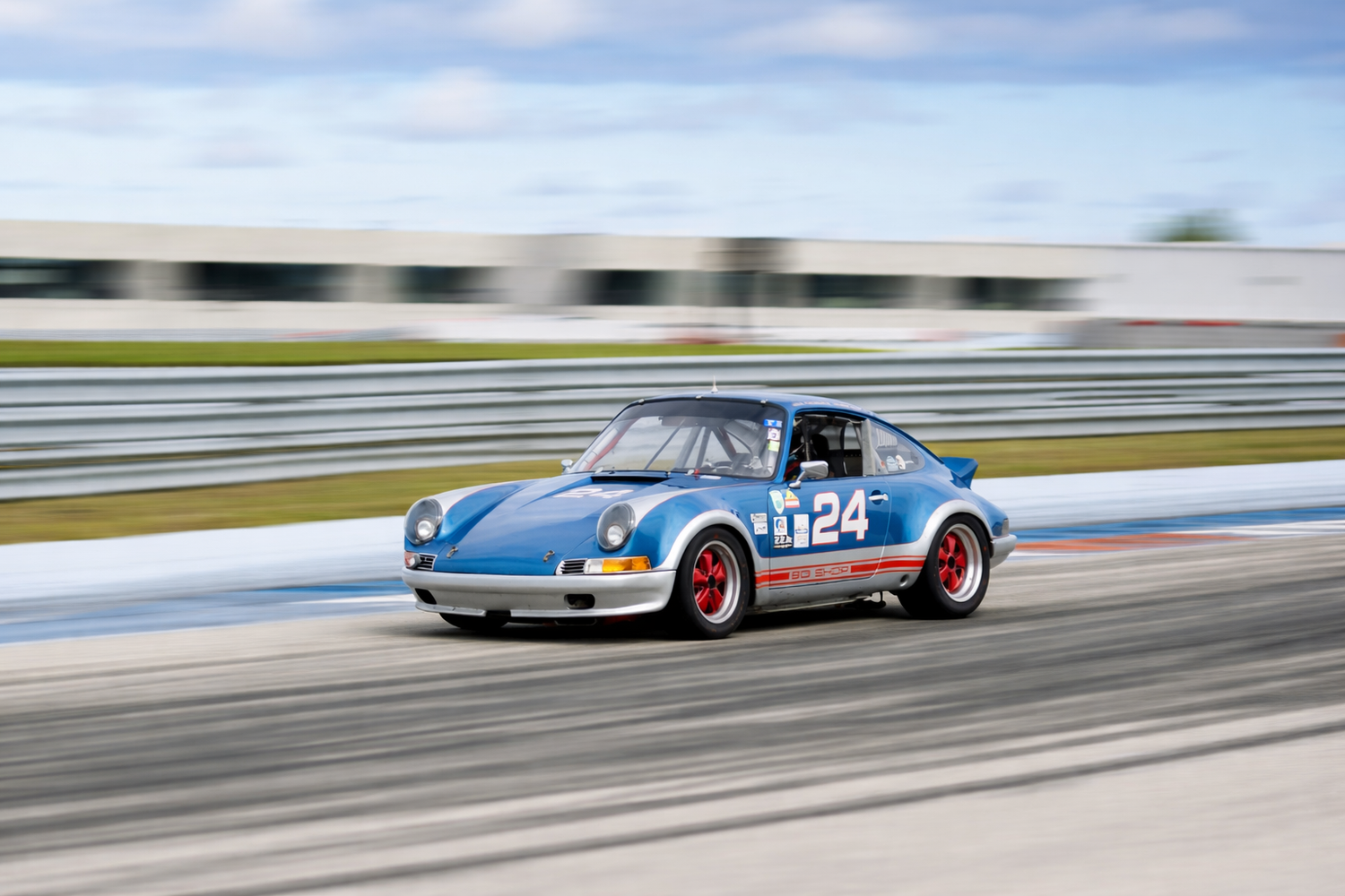 Blue Porsche 911 race car number 24 competing on a circuit track under clear skies.
