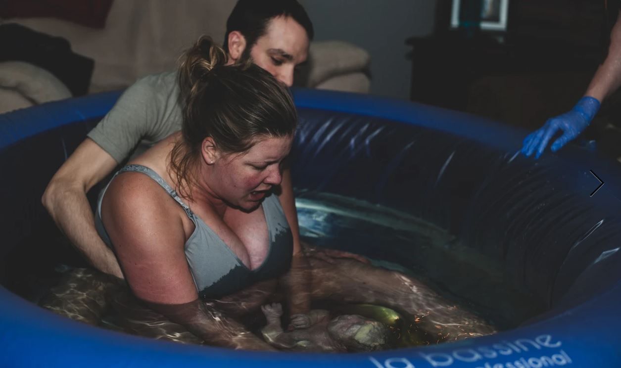 An intimate home birth moment in a blue inflatable birthing pool.
