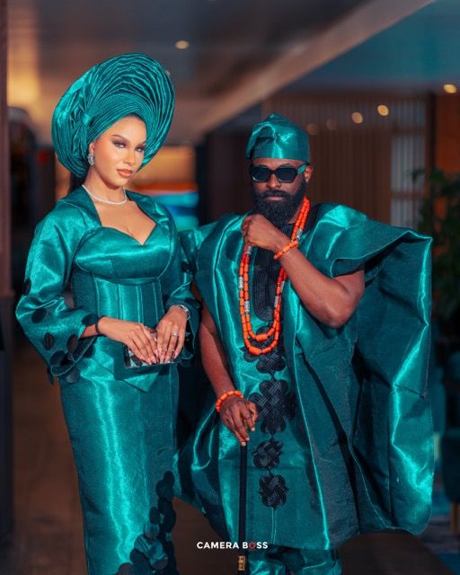 Couple in matching teal traditional Nigerian attire posing together at formal event with elegant gele headwrap and agbada.