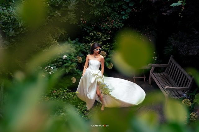 Elegant white wedding dress flowing in a lush garden setting with a wooden bench visible in the background.
