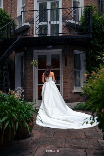 Elegant white wedding gown with dramatic cathedral train photographed from behind against a historic brick building entrance.