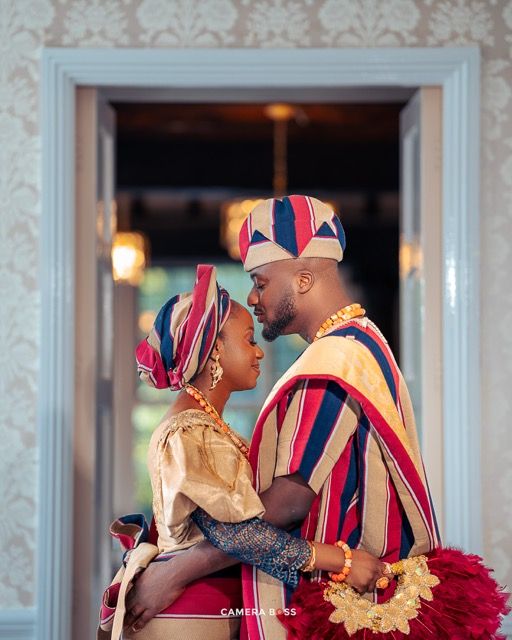 A couple in traditional African wedding attire with vibrant striped fabric embrace intimately during their special celebration.