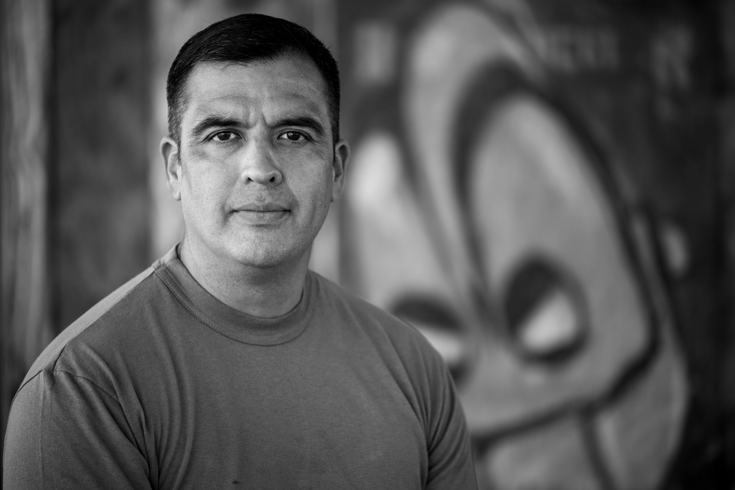 Black and white portrait of a serious man in a t-shirt with graffiti mural background.