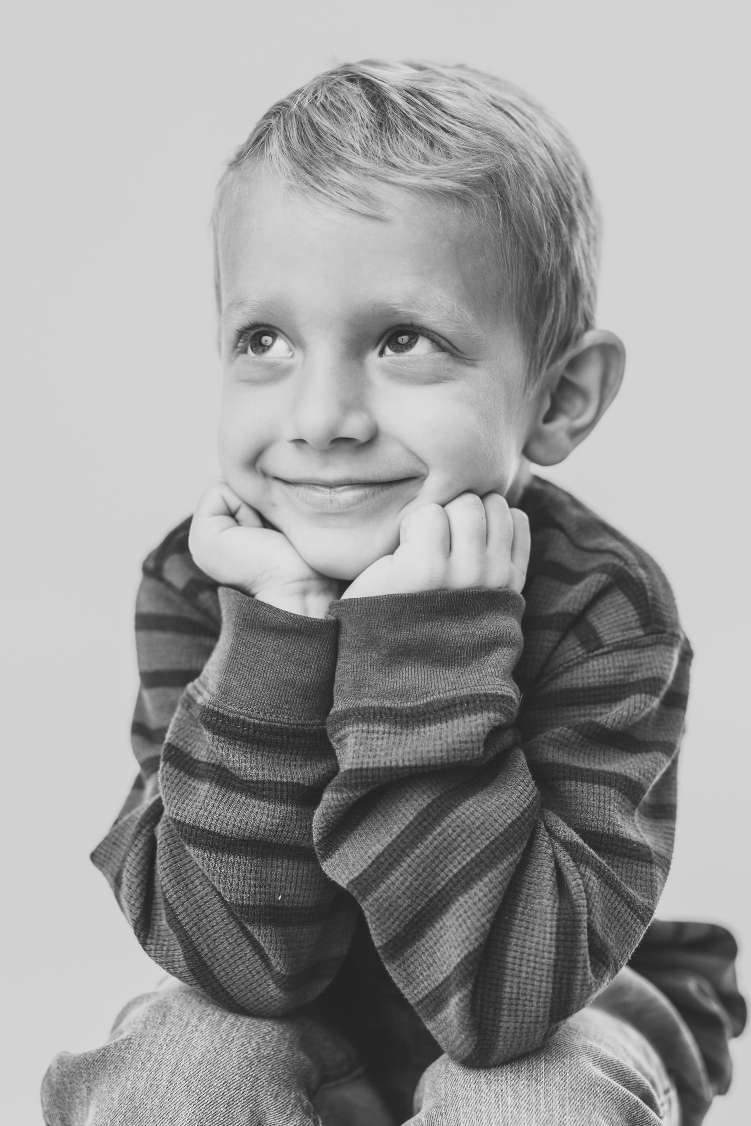 Black and white portrait of a child with curly hair in a dark sweater looking thoughtfully upward.