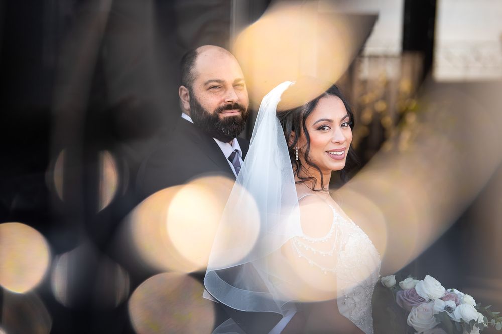 Dreamy bokeh portrait of smiling bride and groom captured through soft circular light reflections.