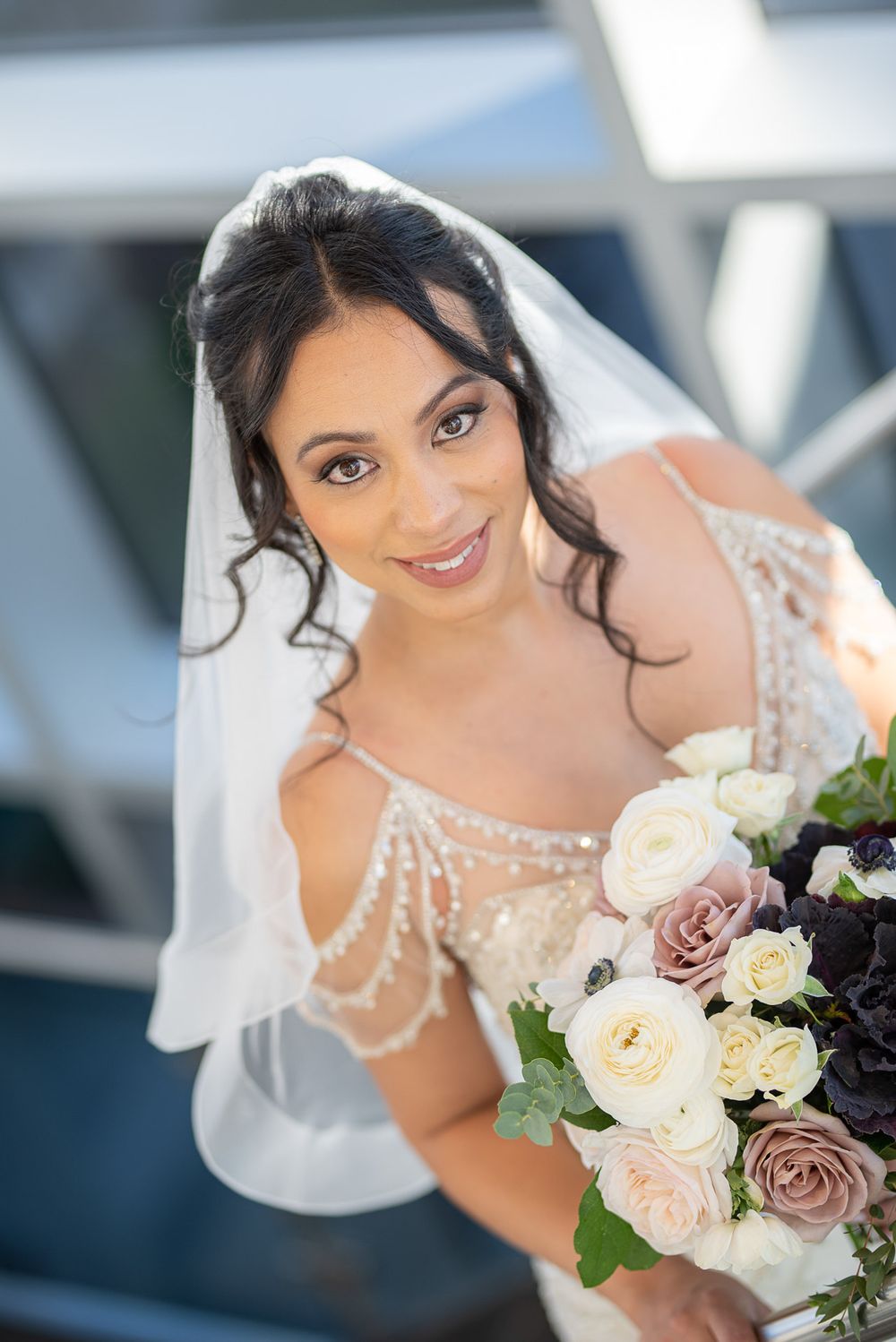 Close-up of smiling bride in a beaded gown holding a soft pink and white bouquet.