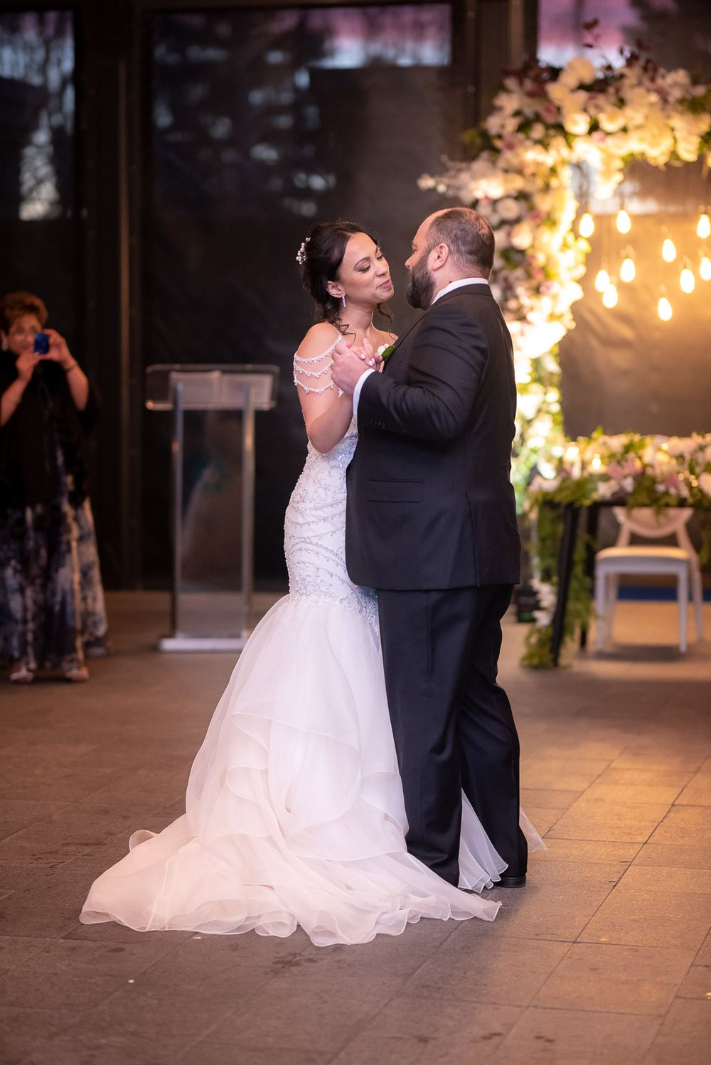 Bride and groom share romantic first dance in front of floral wedding backdrop.