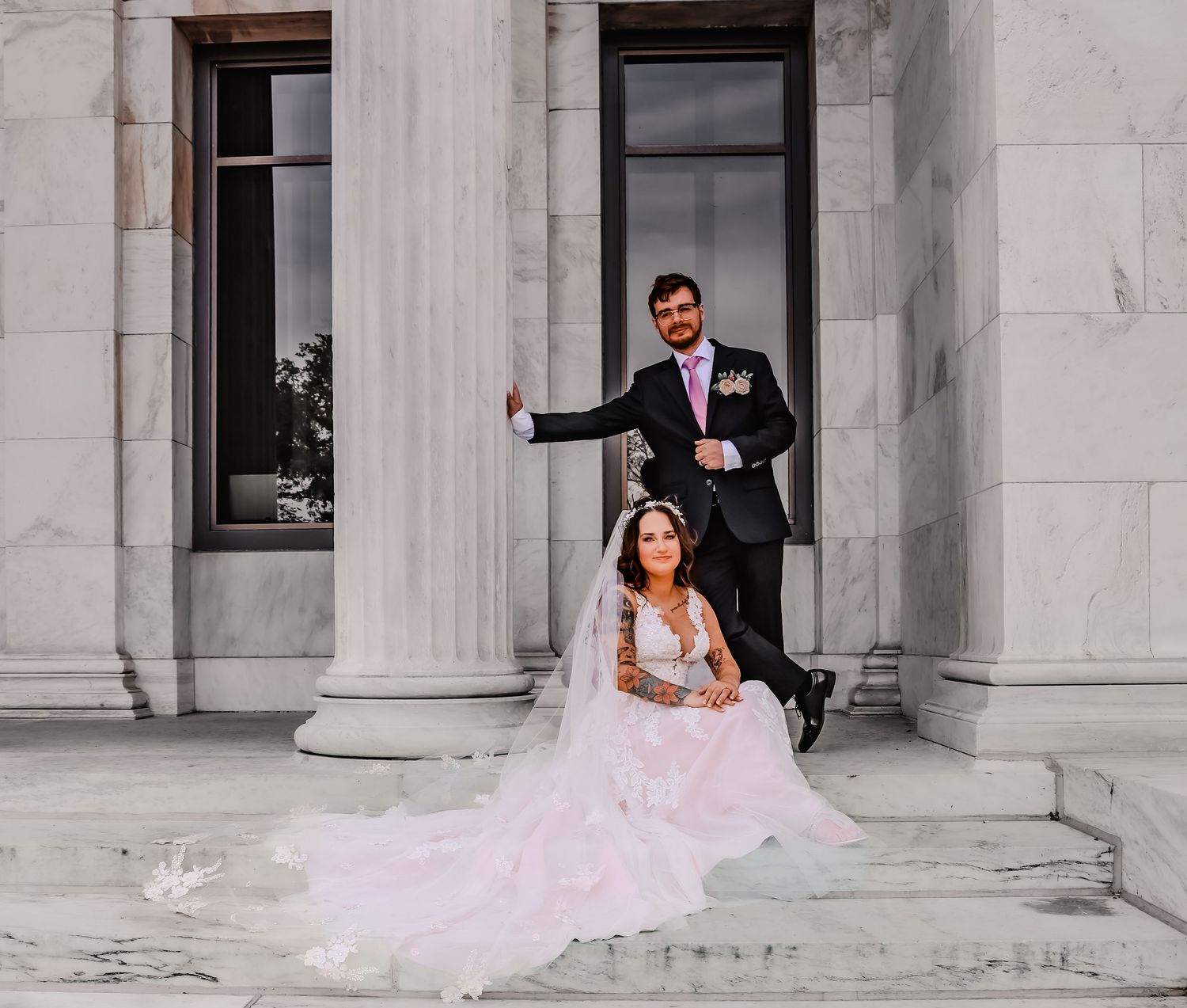 Wedding couple posing on grand stone steps of classical building.