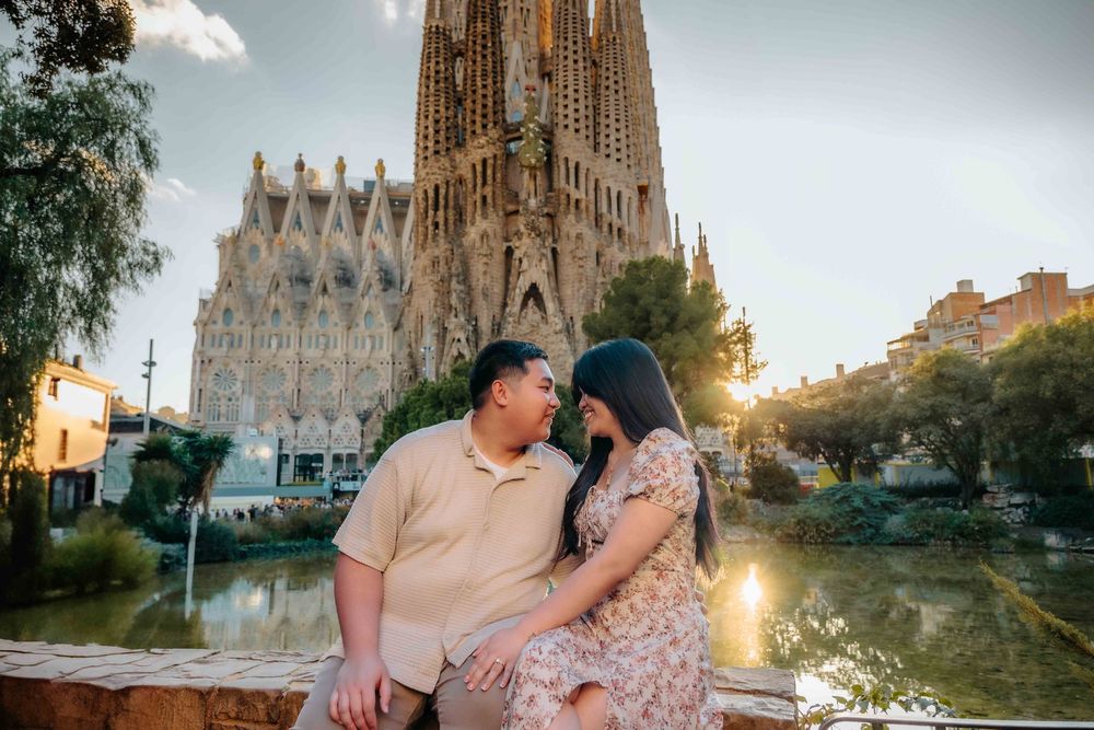 Couple holding hands walking through the park with Sagrada Família background.