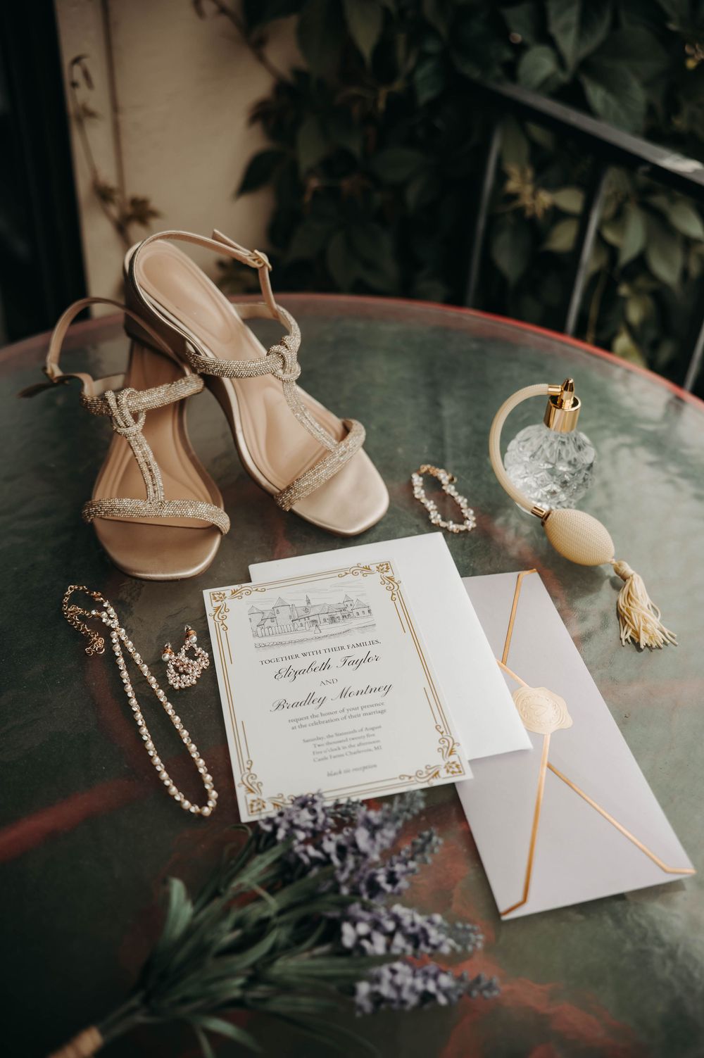 Elegant wedding flat lay featuring gold-trimmed invitations, strappy heels, pearl jewelry, and lavender flowers.