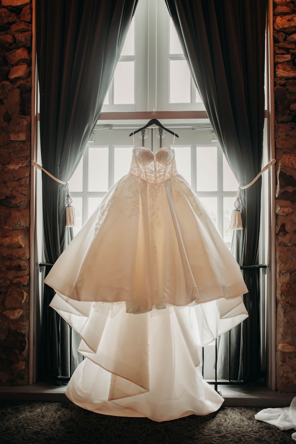 Stunning strapless layered ball gown wedding dress displayed hanging in a sunlit window.