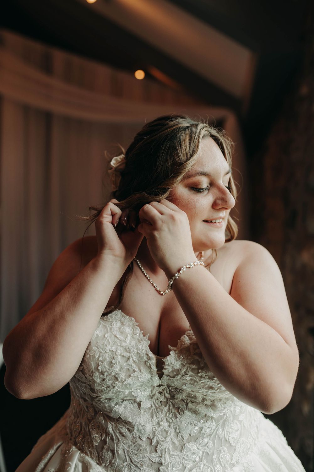 Bride in lace strapless wedding gown putting on earrings while getting ready for her wedding day.