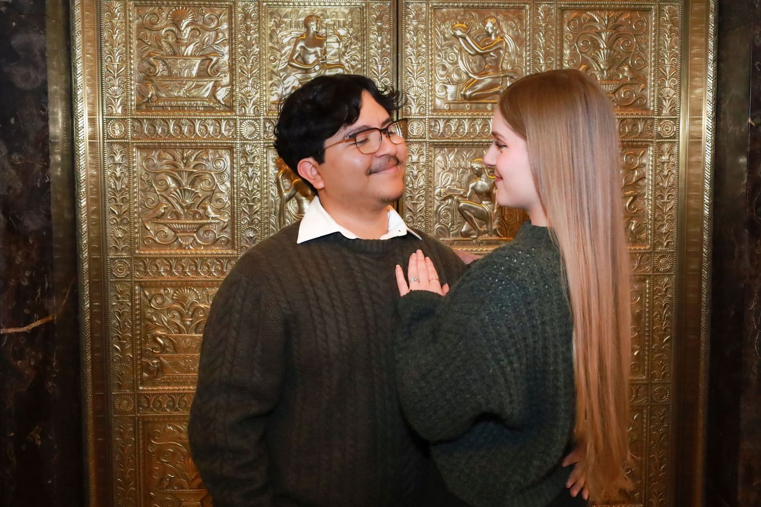 A couple shares an intimate moment in front of a decorative gold metallic wall.