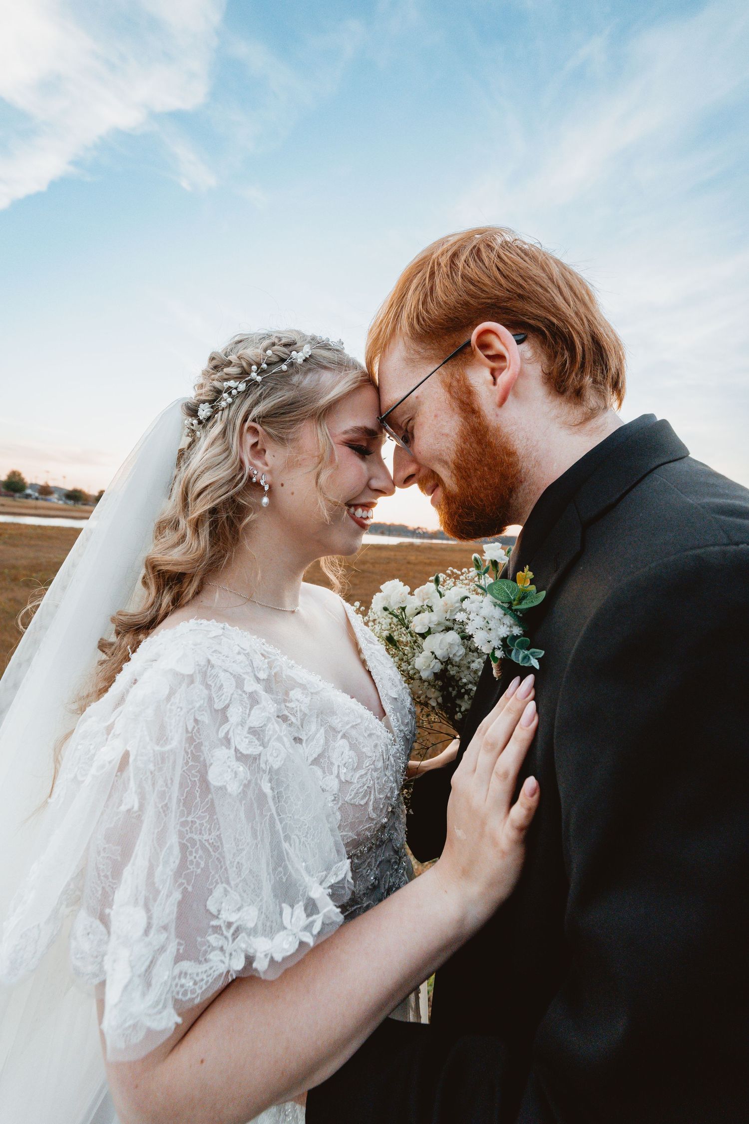 A bride and groom share an intimate moment outdoors with a cloudy sky backdrop in a series of romantic wedding photos.