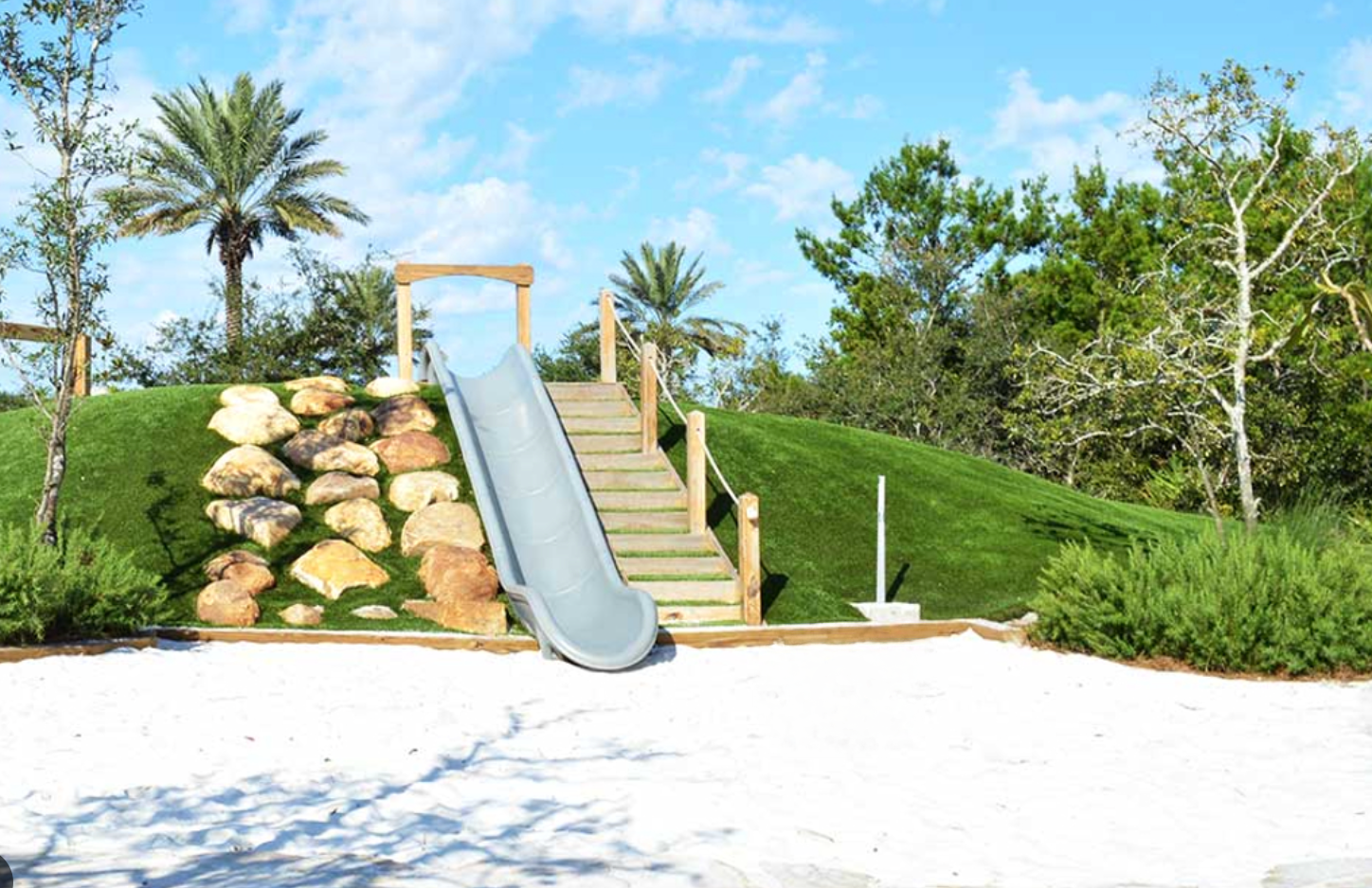 A scenic beachfront walkway with palm trees and lush greenery leads to stairs overlooking the ocean.