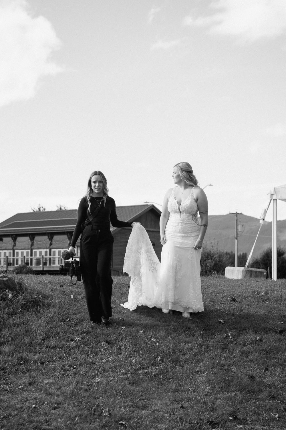 Black and white photo of figures walking across a grassy hillside with buildings in the background.