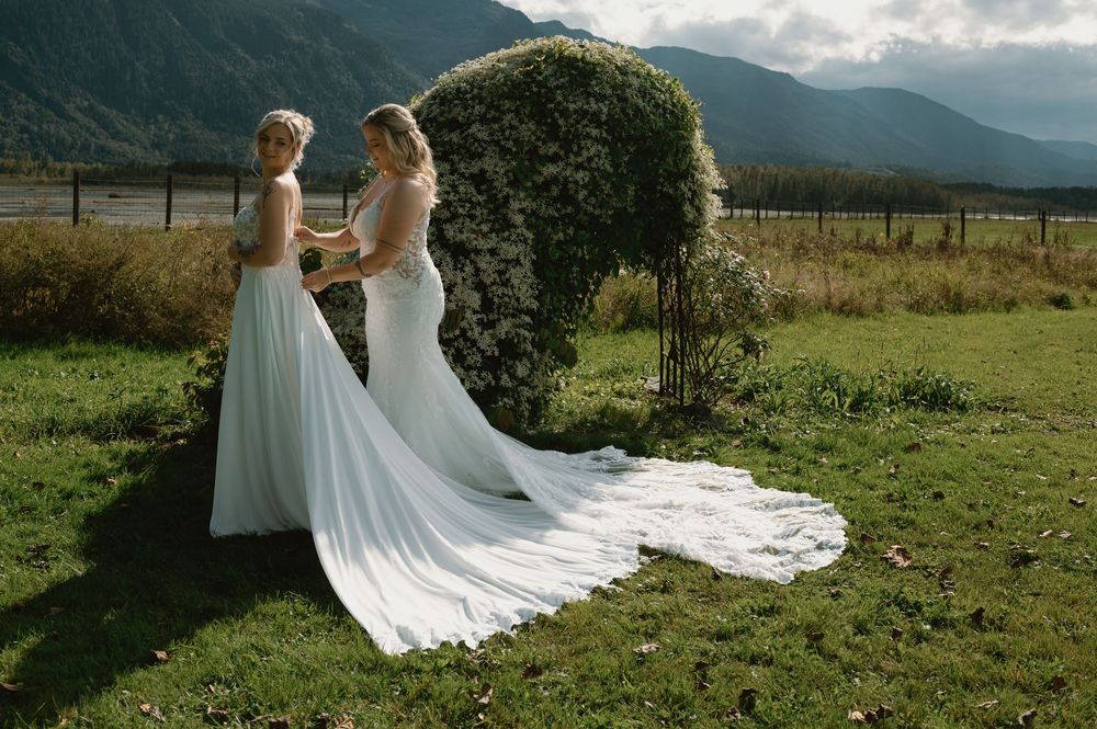 Wedding dresses flowing in the breeze against a mountainous landscape backdrop.