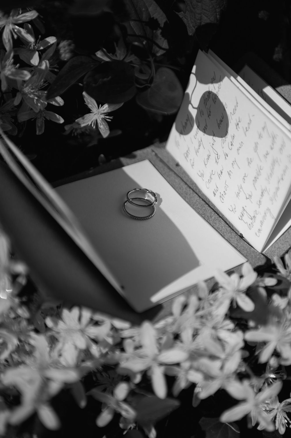 Wedding rings and handwritten vows displayed among delicate white flowers in black and white.