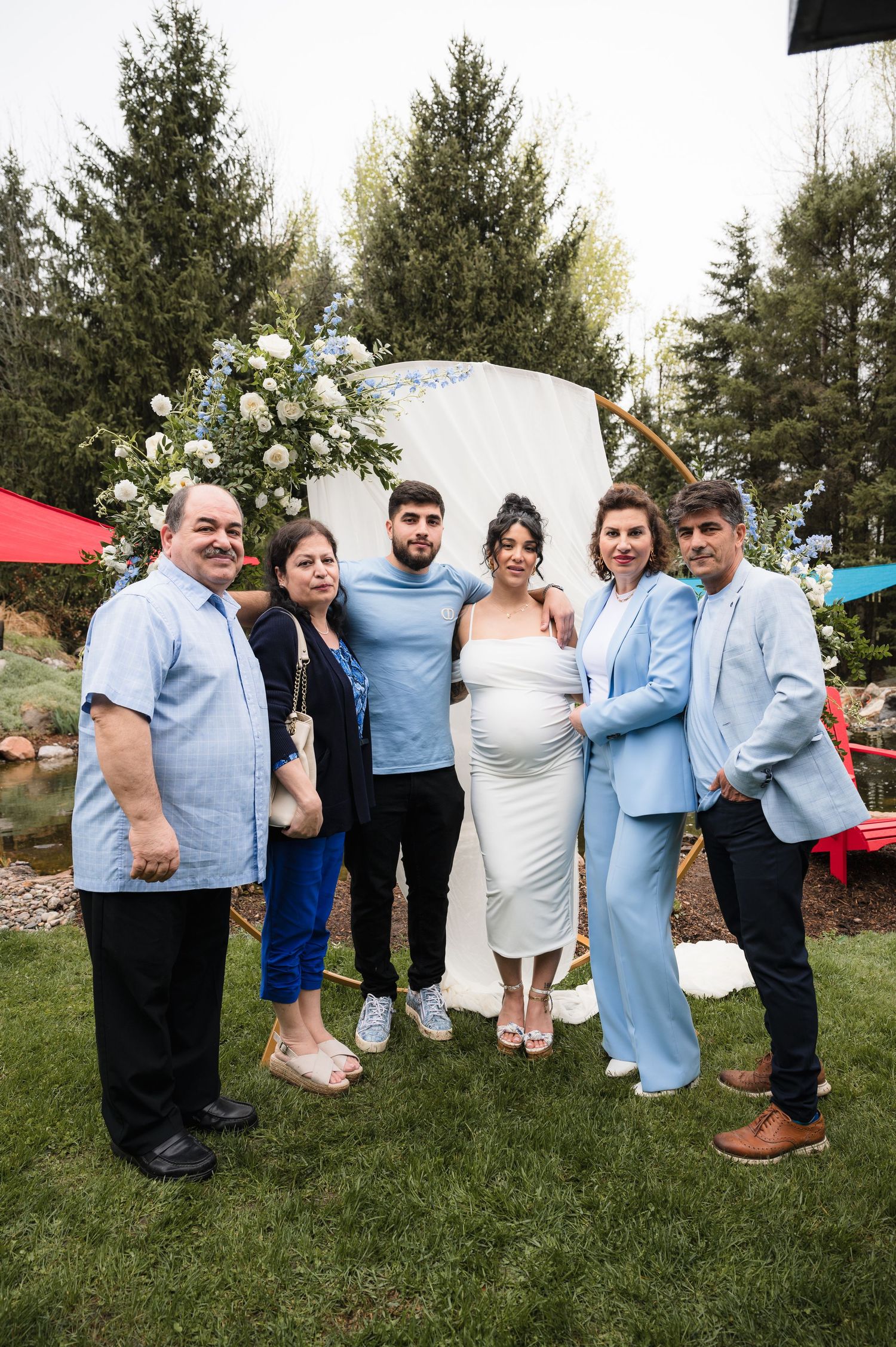 Wedding party poses playfully for photos in matching light blue outfits on grassy lawn during outdoor celebration.